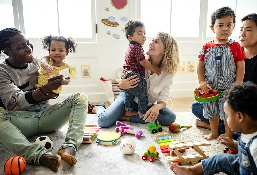 Un papa seul et une maman seule jouant avec leurs enfants dans une salle de jeux commune